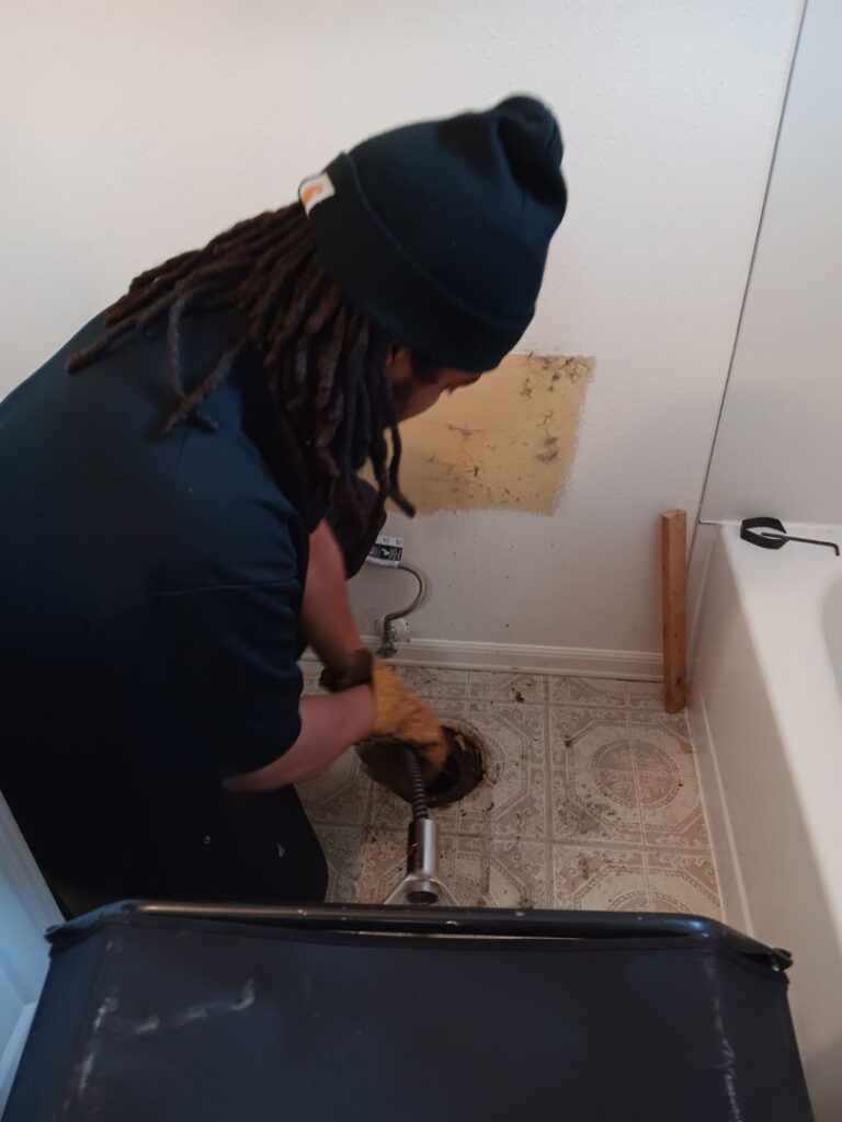 A DNA Drain Cleaning & Sewer technician using a drain snake in a water-damaged bathroom in Tulalip, WA.