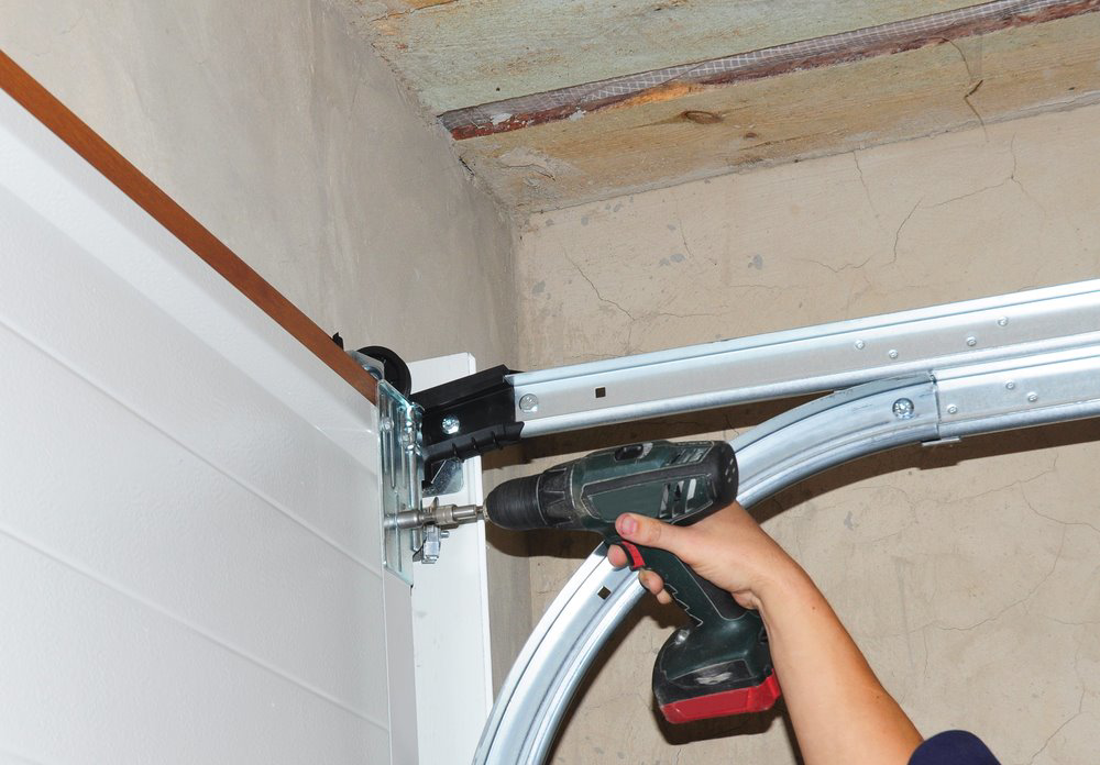 A technician drilling into a garage door track during an installation or repair by Arrow Garage Door in Salt Lake City, UT.