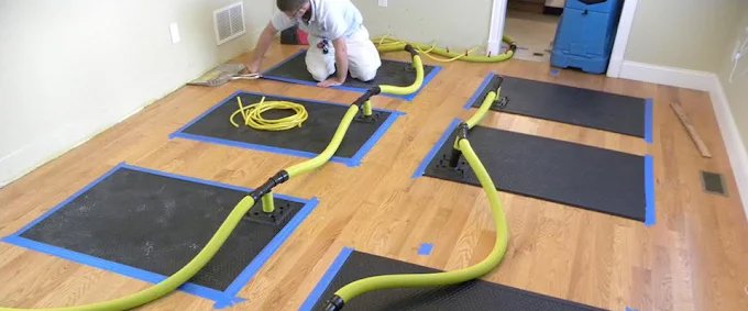 A technician using specialized drying mats and hoses to dry a hardwood floor after water damage at Star Water Damage Fresno, CA.