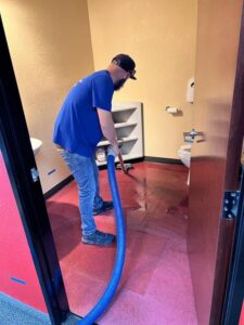 A technician from Lotus Restoration Services extracting standing water from a bathroom floor during a water damage cleanup in Gilbert, AZ.