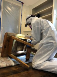 A Green Home Solutions technician in protective gear inspecting furniture for mold or water damage in Mount Airy, MD.