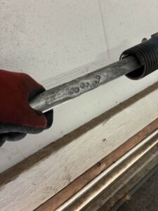 A technician's gloved hand inspecting a garage door torsion spring shaft, indicating repair or maintenance by Carmichael Garage Door in Carmichael, CA.
