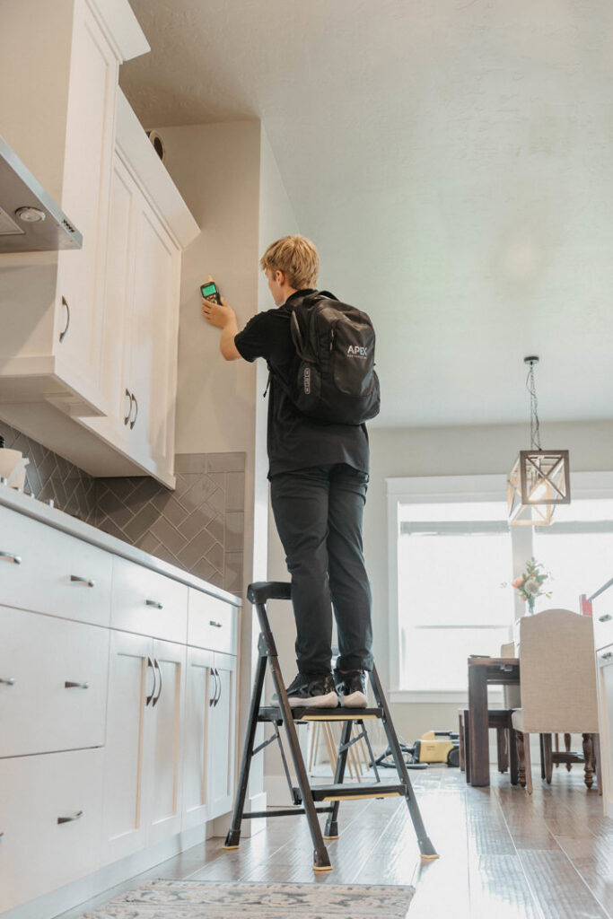 A technician inspecting a kitchen wall for hidden moisture with specialized equipment for APEX Restoration in Mililani, HI