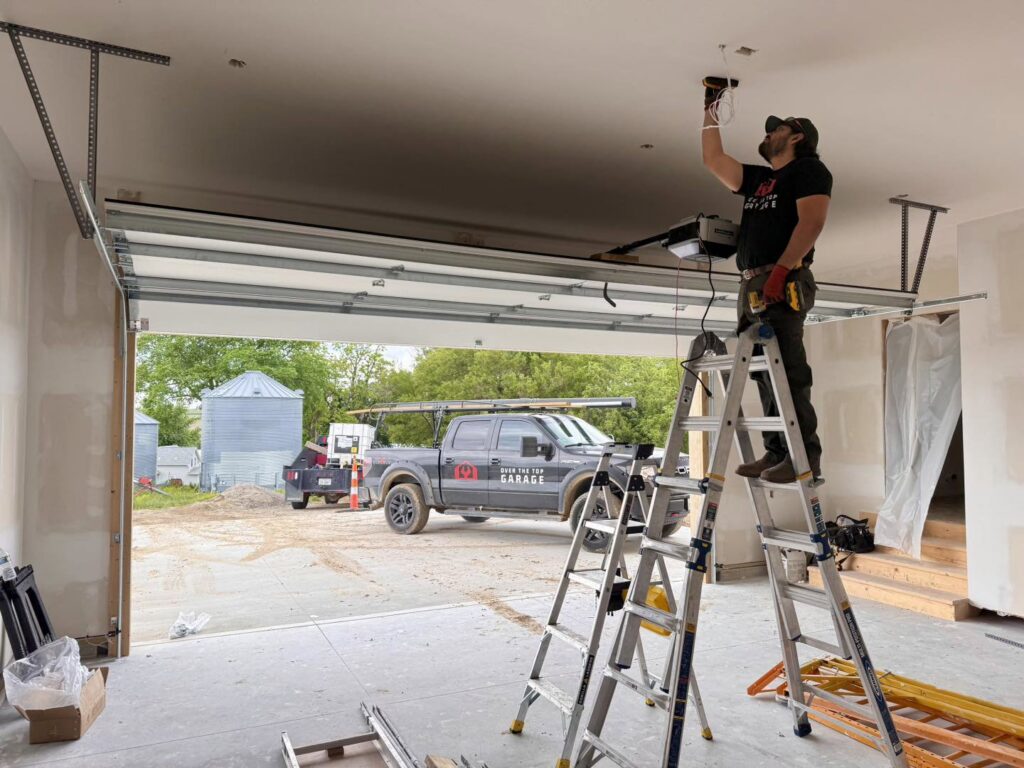 A technician from Over The Top Garage installing a garage door opener, with their service truck visible outside in Albuquerque, NM.