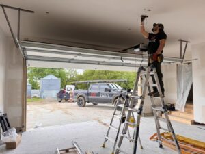 A technician from Over The Top Garage installing a garage door opener, with their service truck visible outside in Albuquerque, NM.