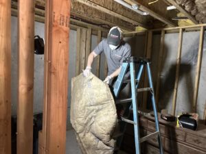 A technician from Level Creek Property Restoration installing insulation in a basement during a property restoration project in Buford, GA.