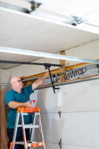 A technician on a ladder lubricating garage door parts during a service call by Bob McDonald Garage Door LLC in Columbus, NE.