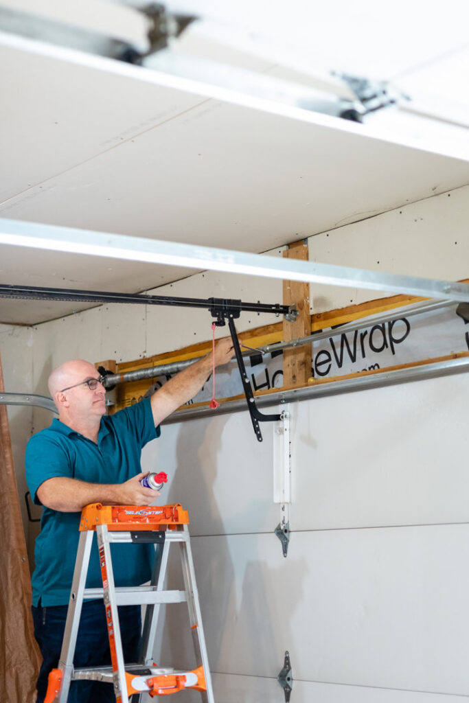 A technician on a ladder lubricating garage door parts during a service call by Bob McDonald Garage Door LLC in Columbus, NE.