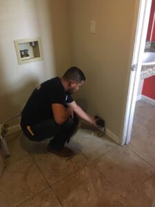 A technician from EZ Water Damage Restoration Services measuring moisture levels in a wall near the floor in Chula Vista, CA.