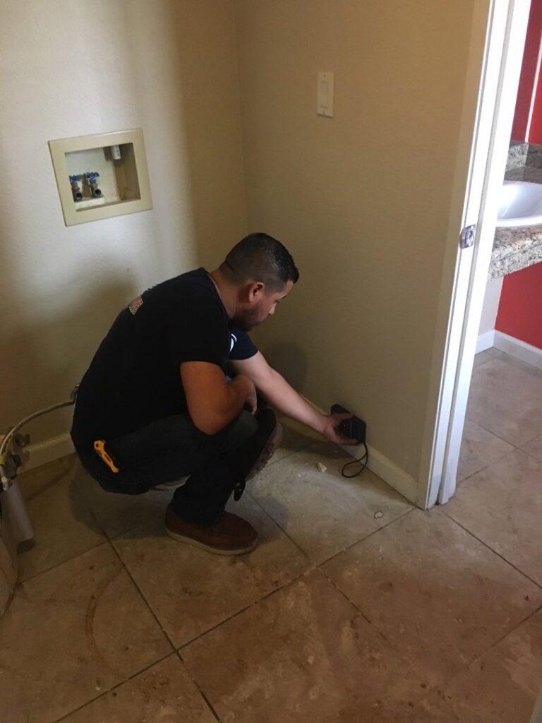 A technician from EZ Water Damage Restoration Services measuring moisture levels in a wall near the floor in Chula Vista, CA.