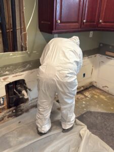 A technician in a protective suit performing demolition and cleanup under a kitchen counter after water damage in Syracuse, UT by Utah Disaster Specialists.