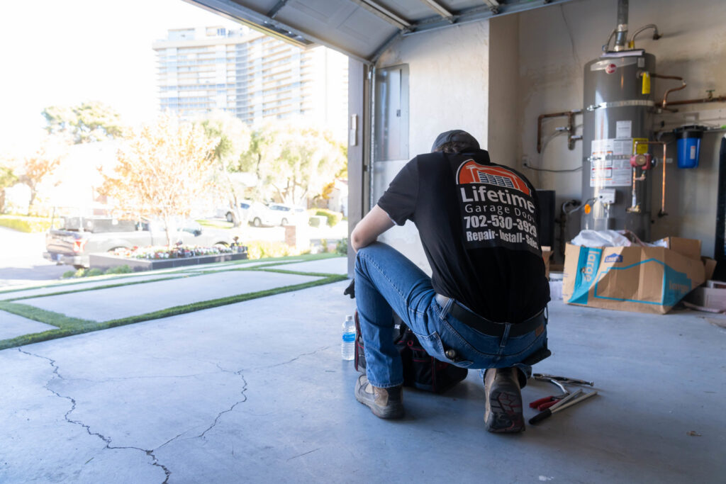 A Lifetime Garage Door technician kneeling with tools inside a garage, preparing for service in Las Vegas, NV.