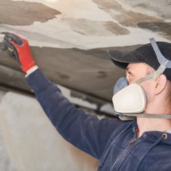 A RestoPros technician wearing a respirator and gloves, removing damaged ceiling material in Norfolk County, MA.