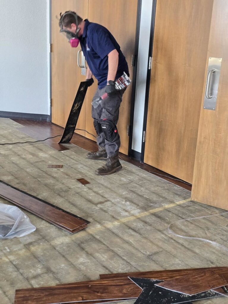 A technician in a respirator removing damaged laminate flooring during water damage remediation by TriForce Restoration in Moore, OK.