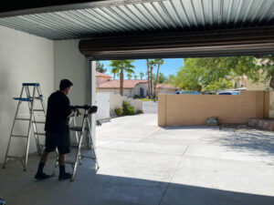 A skilled technician on a ladder performing repair work on a commercial rolling garage door, provided by American Veteran Garage Door Repair Henderson, NV.