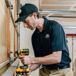 A Precision Garage Door Service of NC technician repairing a garage door panel with a drill in Morrisville, NC.