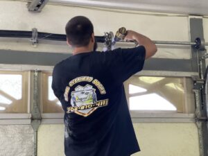 A Rebel Overhead Doors technician repairing a garage door torsion spring assembly with a drill in Las Vegas, NV.