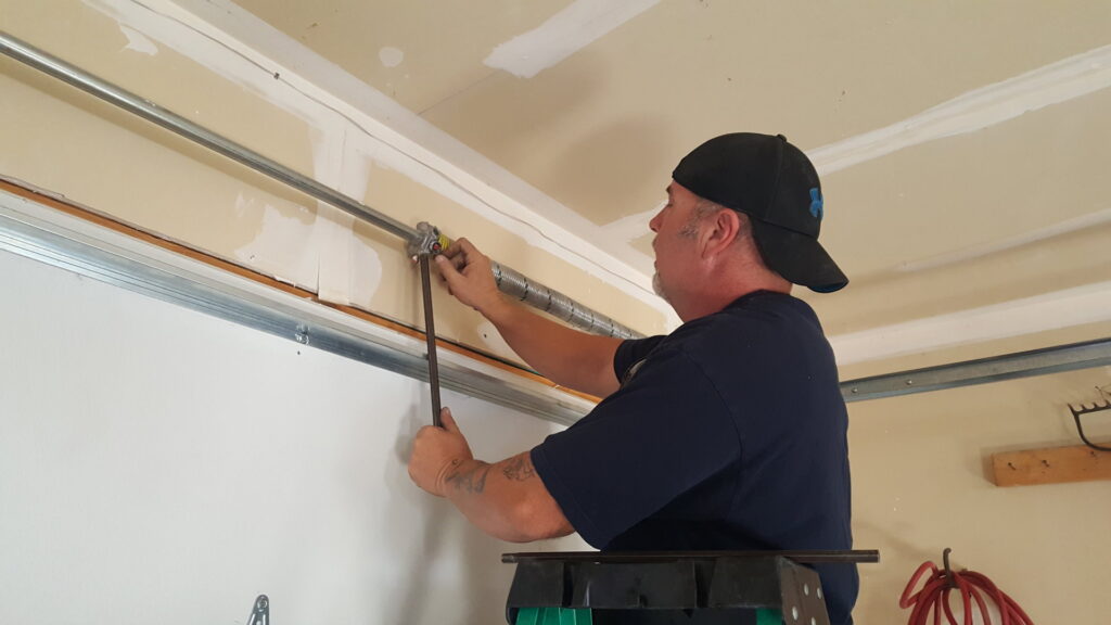A technician repairing a garage door torsion spring system on a ladder for Sandia Garage Door Repair in Albuquerque, NM