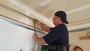 A technician repairing a garage door torsion spring system on a ladder for Sandia Garage Door Repair in Albuquerque, NM