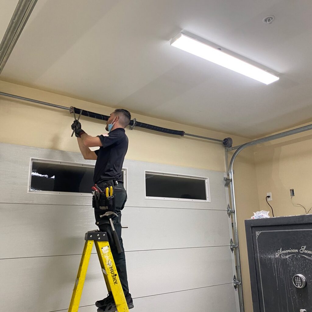 A professional technician on a ladder adjusting or repairing the torsion spring system of a garage door, a service offered by American Veteran Garage Door Repair Henderson, NV.