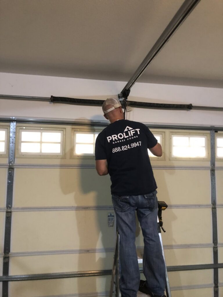 A ProLift Garage Doors of Canyon County technician on a ladder repairing garage door springs and hardware in Nampa, ID.