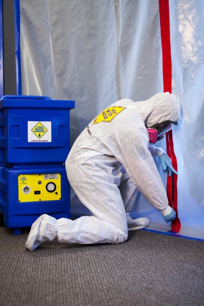A technician in a hazmat suit sealing a containment area during mold remediation by 1-800 WATER DAMAGE of Oklahoma City, OK.