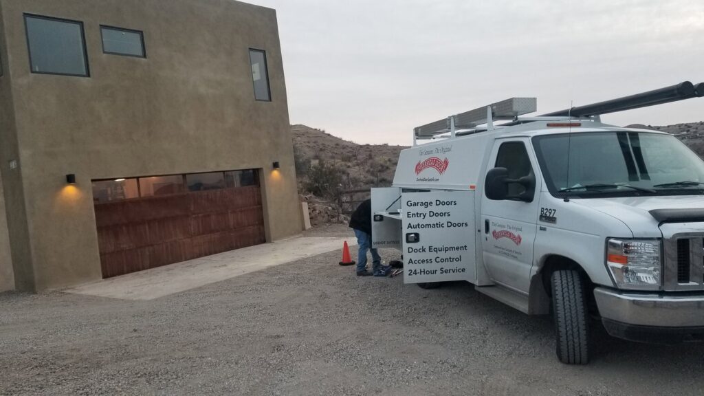 A technician's service van parked at a residential job site with a garage door, indicating work by Overhead Door Company of Albuquerque in Albuquerque, NM.