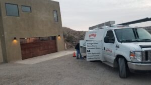 A technician's service van parked at a residential job site with a garage door, indicating work by Overhead Door Company of Albuquerque in Albuquerque, NM.