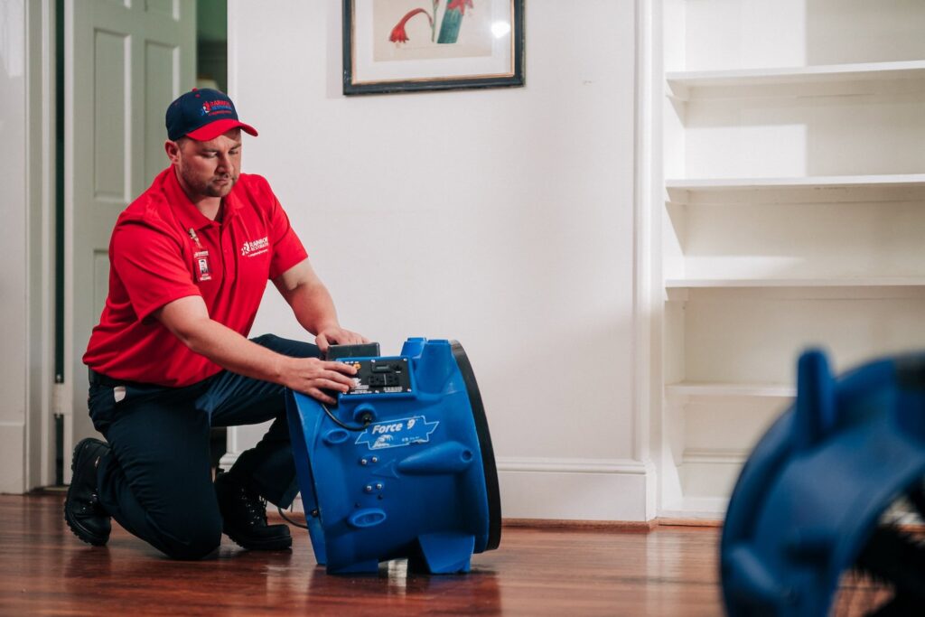 A Rainbow Restoration technician setting up an industrial drying fan on a wooden floor during a water damage restoration job in Clifton Park, NY