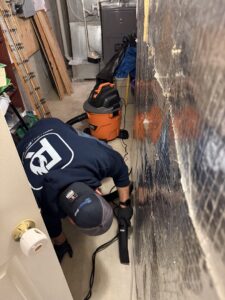 A RestoPros technician extracting water from a damaged wall with a wet vac during a water damage job in Prospect, CT