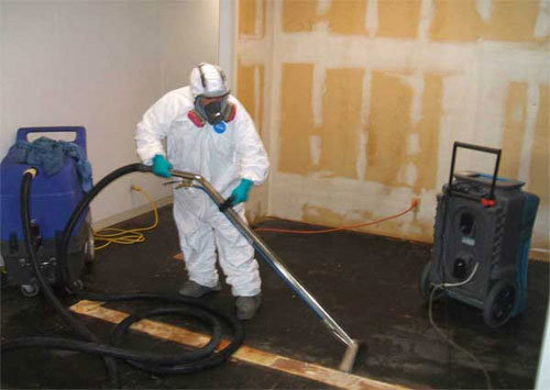 A technician in a hazmat suit using water extraction equipment on a damaged floor for PROTECH Restoration & Cleaning in Philadelphia, PA.