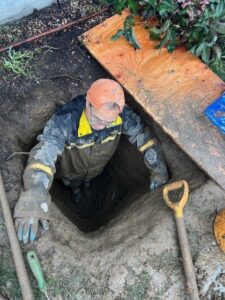 A DNA Drain Cleaning & Sewer technician working in a muddy trench on underground pipes in Tulalip, WA.