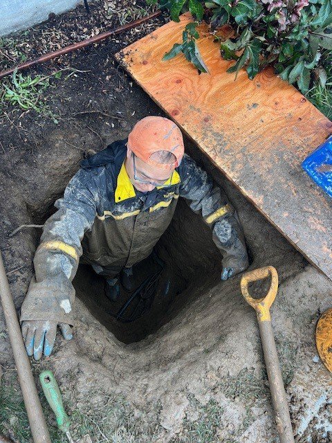 A DNA Drain Cleaning & Sewer technician working in a muddy trench on underground pipes in Tulalip, WA.