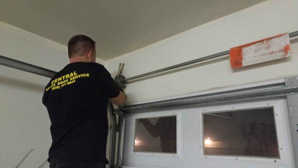 A Central Garage Door Service technician working on a garage door track and roller system in Kapolei, HI.