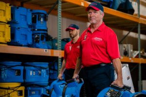 Two technicians from Rainbow International Restoration of Annapolis, MD, carrying blue air movers, essential equipment for water damage restoration.