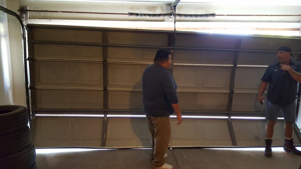 Two technicians inspecting a damaged and bent garage door, assessing the repair needs for Sandia Garage Door Repair in Albuquerque, NM