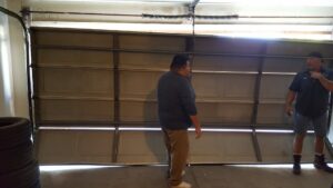 Two technicians inspecting a damaged and bent garage door, assessing the repair needs for Sandia Garage Door Repair in Albuquerque, NM