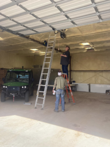 Two technicians installing a garage door opener mechanism inside a commercial garage for Doors & more,inc in Quincy, IL