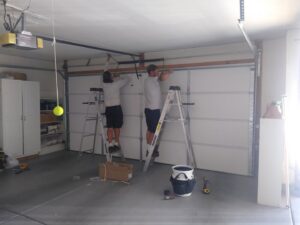 Two Garage Door Mesquite technicians on ladders performing installation or repair work on a residential garage door in Mesquite, NV.