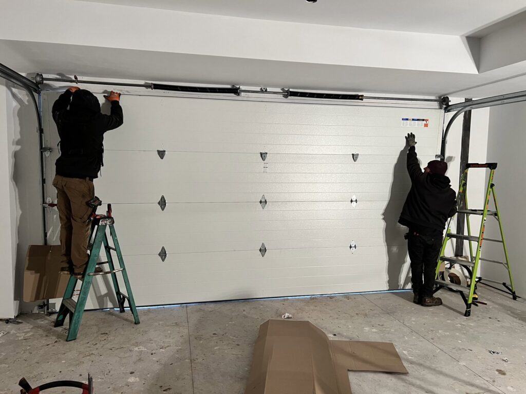 Two technicians from Right Choice Doors installing a new white garage door inside a residential garage in Layton, UT.