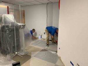 Two technicians from Lotus Restoration Services removing damaged drywall during a water damage or mold remediation project in Gilbert, AZ.