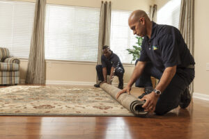ServiceMaster technicians rolling up a wet rug from a hardwood floor during water damage cleanup in Lexington, KY.