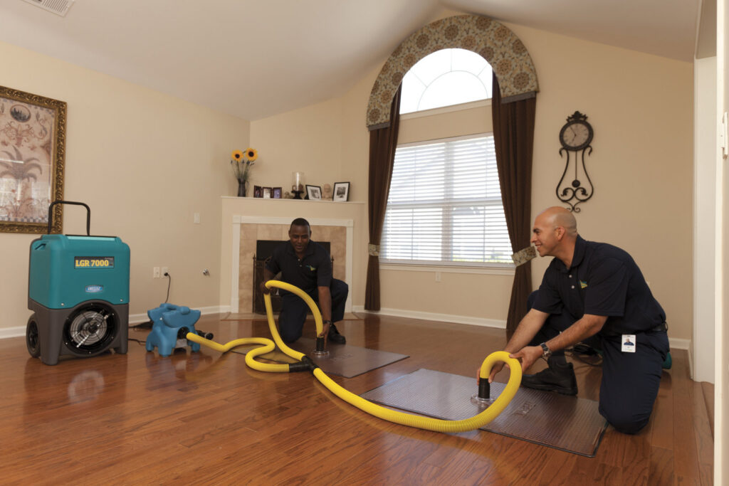 ServiceMaster technicians performing water extraction on a hardwood floor in a living room in Lexington, KY.