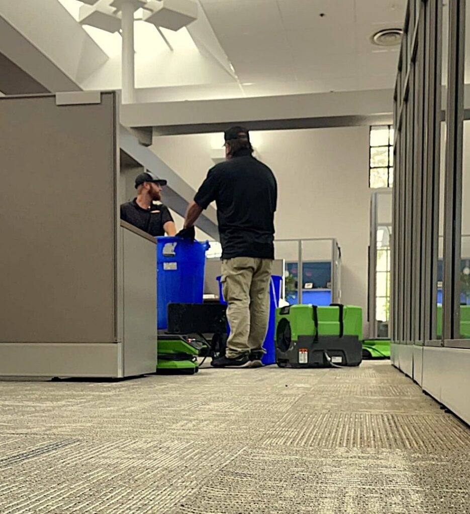 SERVPRO technicians working in an office with blue bins and green air movers, indicating water damage cleanup and drying in Alexandria, LA.