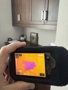 A thermal imaging camera detecting hidden moisture behind a wall during a water damage assessment by Flow State Restoration in Gilbert, AZ