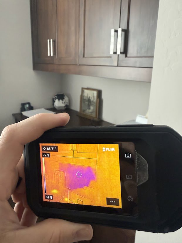 A thermal imaging camera detecting hidden moisture behind a wall during a water damage assessment by Flow State Restoration in Gilbert, AZ