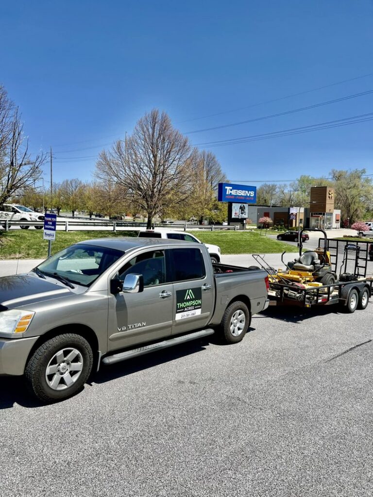 A Thompson Acres branded pickup truck pulling a trailer with professional lawn care equipment in Davenport, IA.