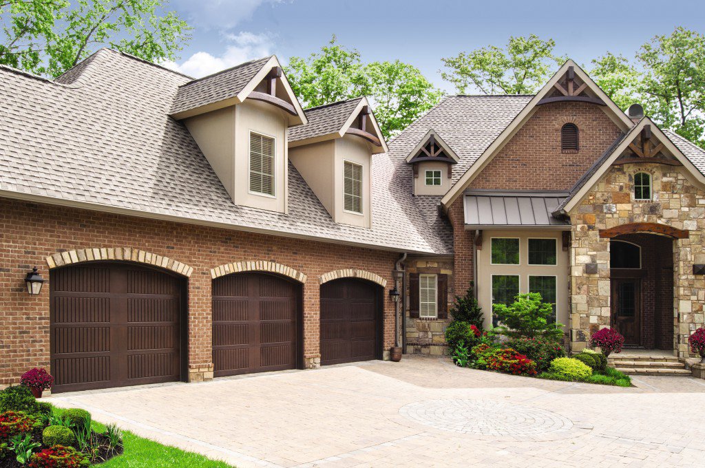 Three arched dark brown garage doors installed on a brick house by Wayne Dalton Sales & Service of Quad Cities in Davenport, IA.