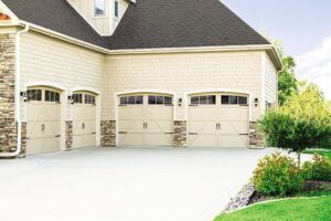 Exterior of a house featuring three beige garage doors, two with decorative hardware and windows, by Pioneer Overhead Door, Inc in Las Vegas, NV.