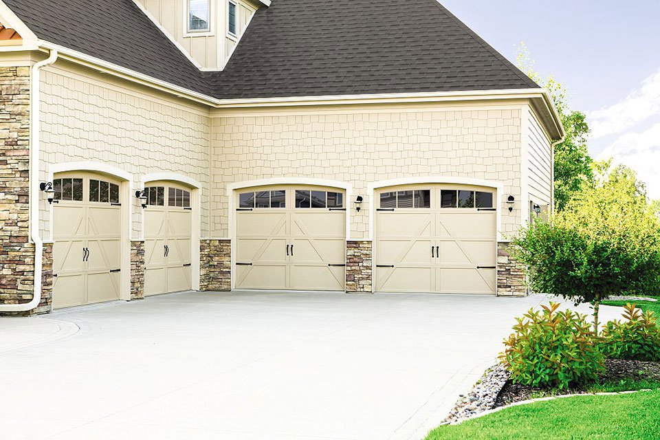Exterior of a house featuring three beige garage doors, two with decorative hardware and windows, by Pioneer Overhead Door, Inc in Las Vegas, NV.